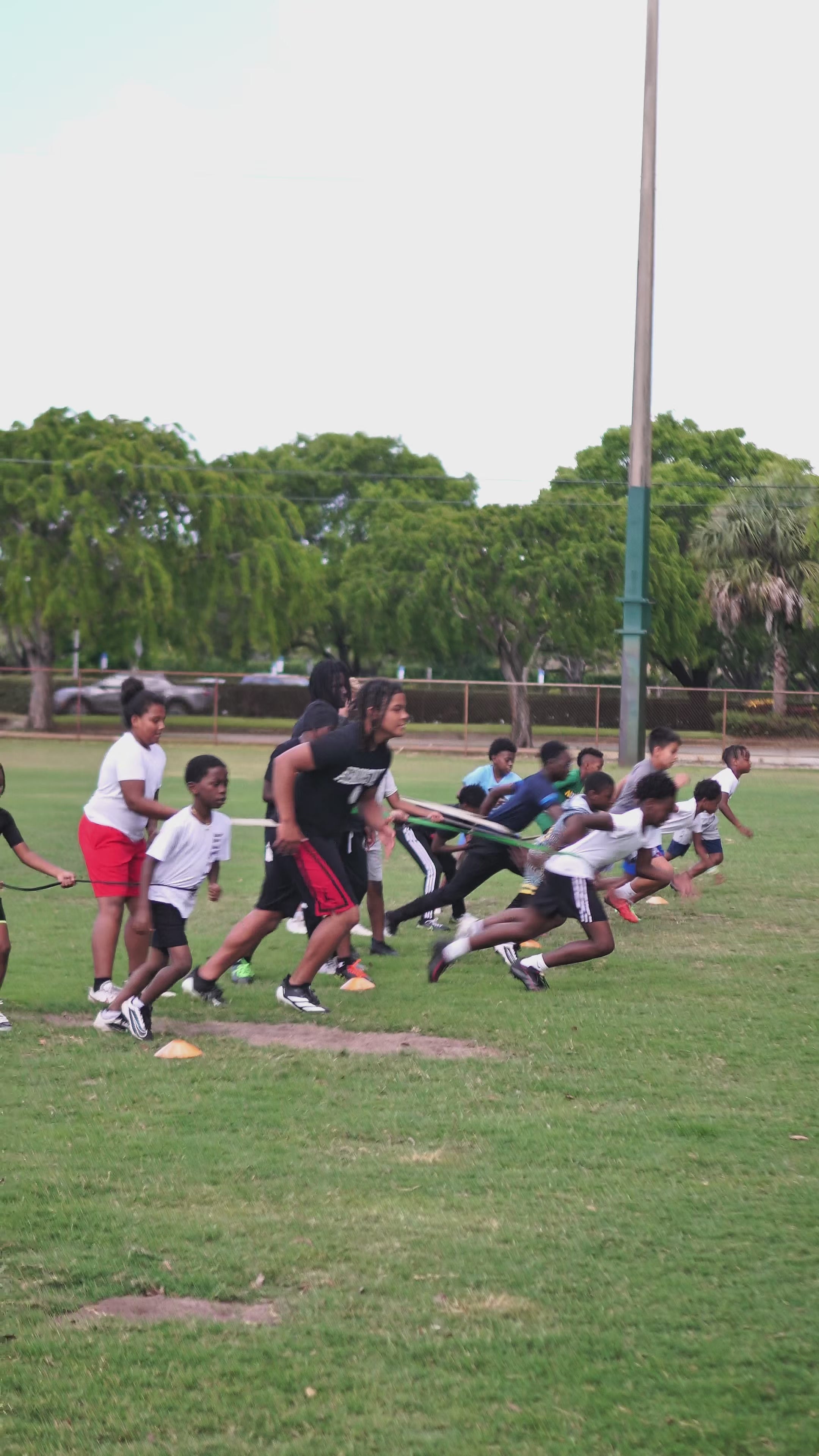 Load video: Dynamic training session with diverse youth athletes performing agility ladder drills, medicine ball exercises, and resistance band sprints. Coach provides hands-on technique correction as athletes demonstrate focus and determination in improving their athletic performance. High-energy workout showcasing proper form and progressive training methods for youth sports development